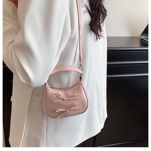 Mini sac demi-lune rose avec nœuds porté par un mannequin en tenue blanche élégante