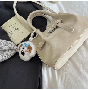 Détail du sac seau mat crème avec un charmant pendentif chien en peluche sur un tissu