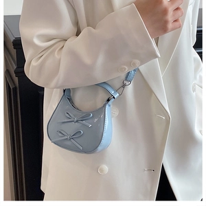 Gros plan d'un mini sac à main croissant bleu clair avec doubles nœuds et finition vernie