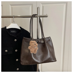 Detail of dark brown leather tote bag with metallic buckle and plush bear charm