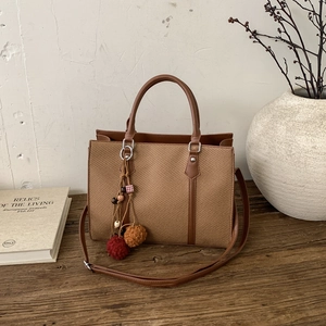 Detail of vintage woven tote bag with leather straps and decorative tassel on a wooden desk