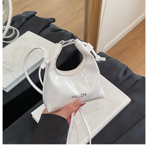 Detail of white glossy patent leather handbag with curved handle and knotted strap