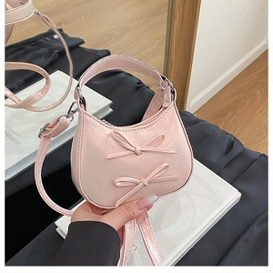 Détail d'un mini sac demi-lune rose en cuir verni avec des nœuds doux et une poignée