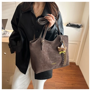 Detail of dark brown vintage faux leather tote bag featuring white stitching and bear charm
