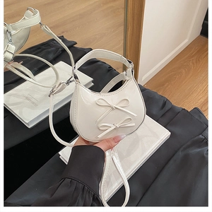 Détail du sac demi-lune blanc avec nœuds décoratifs et finitions métalliques
