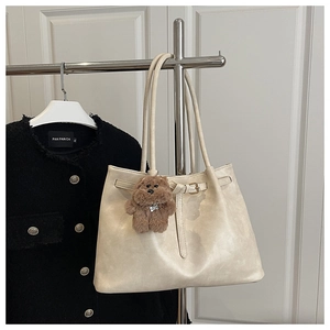 Detail of beige tote bag with buckle strap, plush teddy bear charm and sleek shoulder strap