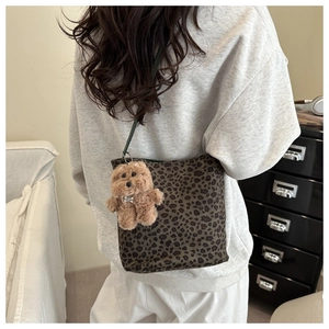 Chic leopard print bucket bag with plush dog charm worn by model in a modern room