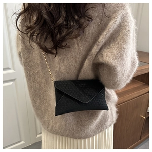 Detail of a black woven envelope crossbody bag with a delicate gold chain shoulder strap