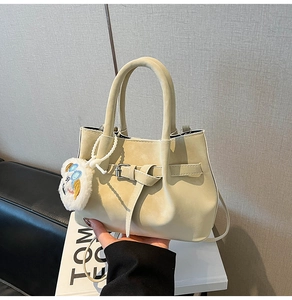 Détail du sac seau en cuir mat beige avec boucle décorative et pendentif peluche