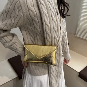 Sac enveloppe doré métallisé avec texture ondulée verticale et fine bandoulière en chaîne