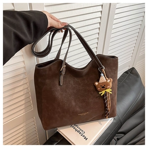 Detail of dark brown leather tote bag with vintage texture and cute bear charm