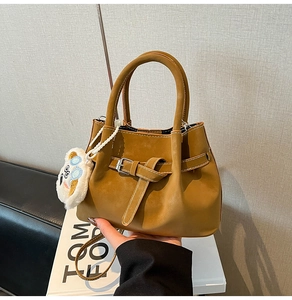 Détail du sac seau en cuir caramel avec poignée supérieure et breloque en peluche
