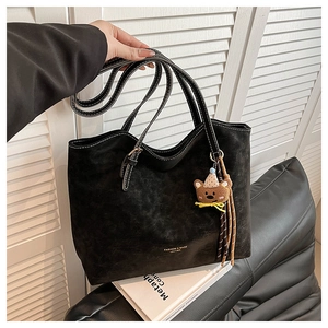 Close-up of black suede tote bag texture with fashion lettering and bear pendant