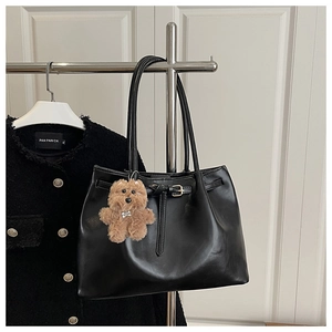 Detail of black tote bag with decorative leather strap and cute brown plush bear charm