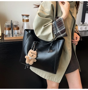 Close-up of black leather tote bag with cute brown plush bear charm for daily commute