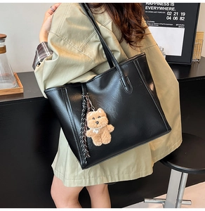 Detail of black PU leather tote bag featuring a cute plush bear charm and woven tassel