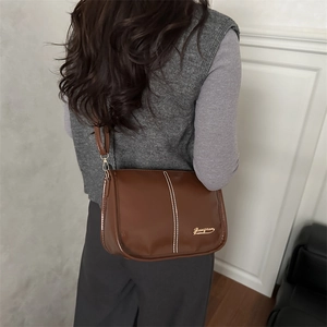 Sac bandoulière marron en similicuir avec coutures blanches et détails dorés sur modèle