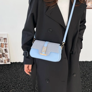 Light blue crossbody bag with gold buckle on a black trench coat model, minimalist style