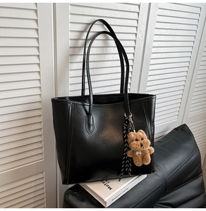 Detail of black faux leather tote bag with plush bear charm and striped silk scarf