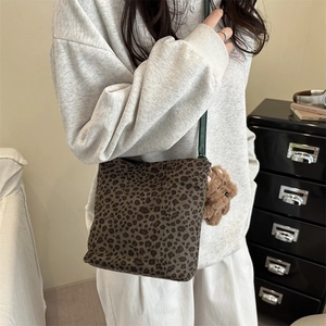 Leopard print crossbody bucket bag with green strap and brown plush bear charm detail