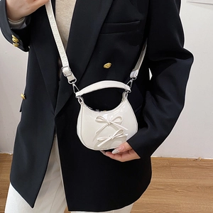Glossy white crescent handbag with bow details and adjustable strap shown on model