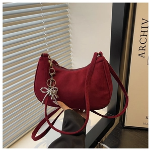 Detail of dark burgundy suede shoulder bag with a silver beaded bow charm pendant