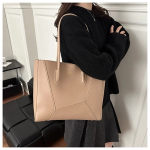 Detail of minimalist beige leather tote bag with geometric stitching and metal logo