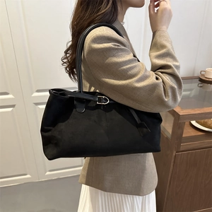 Classic black suede tote bag with golden buckle shown on shoulder for commuting