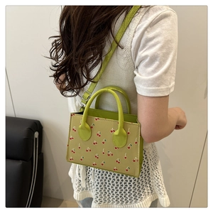 Détail du sac à bandoulière vert imprimé cerises, avec poignée et boucle en métal