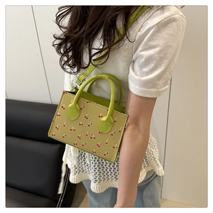 Détail du sac à bandoulière vert à imprimé cerises avec texture cuir et bandoulière