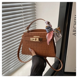 Detail of caramel crocodile pattern Kelly bag with silk scarf on handle and gold buckle