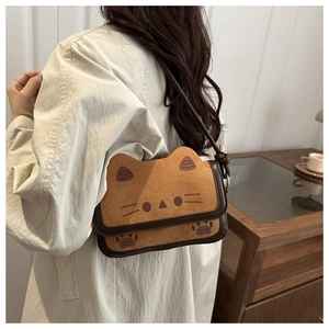 Close-up of a brown suede cat-shaped crossbody bag worn by a model in a cozy setting