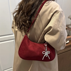Dark red suede crescent shoulder bag with silver bow charm worn by a model in a trench coat