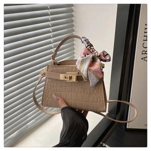 Detail of beige crocodile embossed handbag with gold clasp and decorative pink scarf