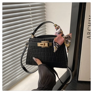 Close-up of black crocodile embossed Kelly handbag with gold twist lock and silk scarf