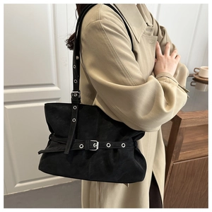 Detail of black suede shoulder bag with silver eyelets and metal buckles on a model