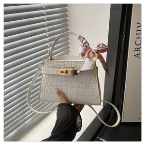 Detail of white crocodile texture handbag with gold twist lock and silk scarf handle