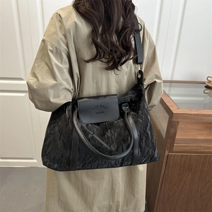 Large black travel bag with pleated texture and adjustable strap worn by a female model