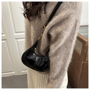Detailed view of black patent leather hobo bag with gold hardware worn by model