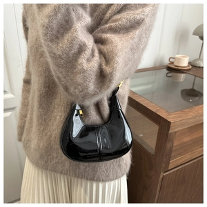 Detail of black patent leather crescent bag with elegant gold zipper and hobo stitching