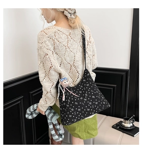 Détail d'un sac bandoulière en toile noire avec nœuds blancs et breloque peluche rose