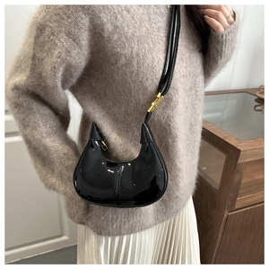 Close-up of a black patent leather crescent shoulder bag with gold hardware on a model