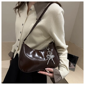 Gros plan du sac hobo marron brillant avec pendentif nœud en strass sur l'épaule