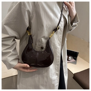 Close-up of a dark brown glossy patent leather crescent bag with gold metal hardware