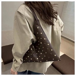 Détail d'un sac à bandoulière triangulaire marron foncé avec clous en métal doré et argenté sur cuir