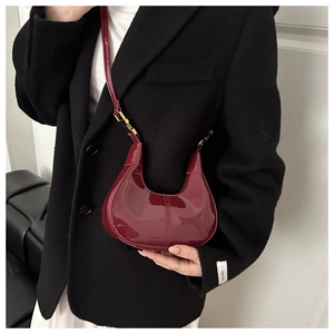 Detail of burgundy patent leather crescent bag with gold hardware on a model