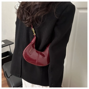 Detail of burgundy patent leather crescent bag worn with gold hardware accents
