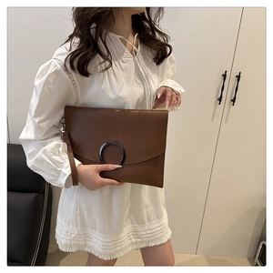 Detail of a brown envelope clutch with black metal ring and wrist strap on white outfit
