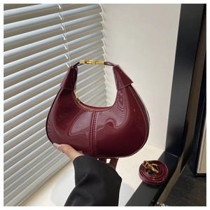Detail of burgundy patent leather crescent bag with gold buckle and glossy finish