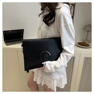Detailed view of black leather envelope clutch featuring a large metallic horseshoe buckle